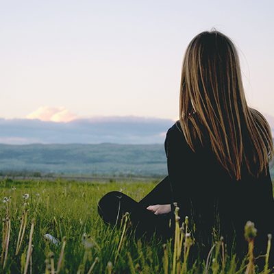 Breathe Well - woman sitting, facing beautiful view of clouds, mountains, and fields